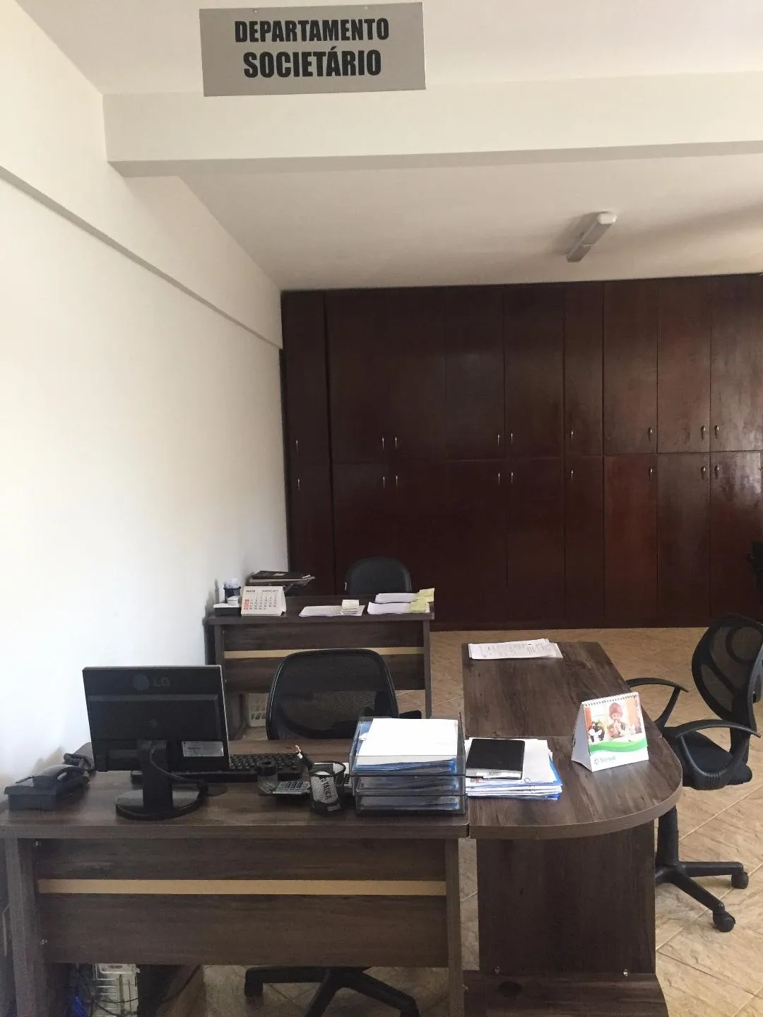 Sala do Departamento Societário, com mesas, computadores e armário de madeira