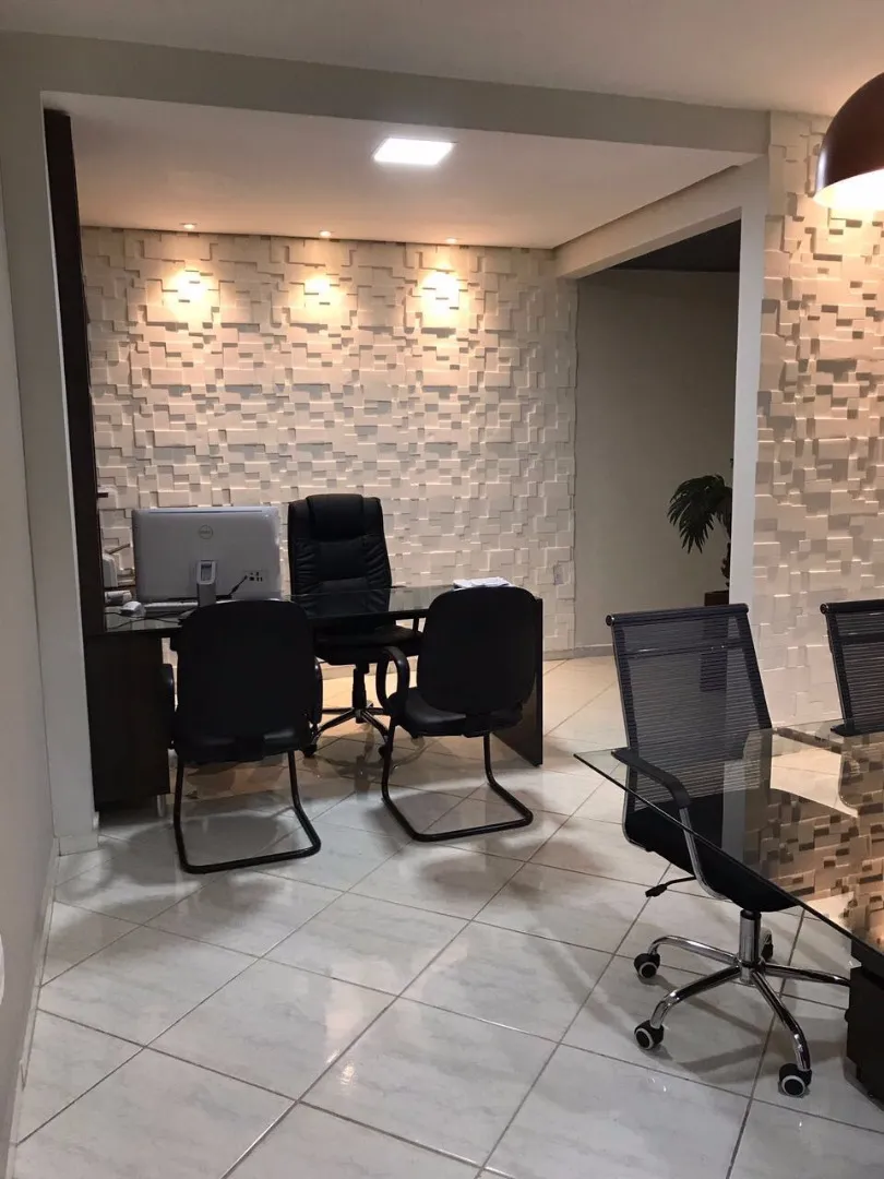 Sala de atendimento com parede de pedra iluminada, mesa com computador e cadeiras